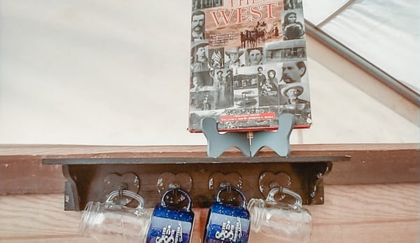 A picture on a shelf with mugs hanging beneath