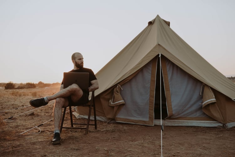 man sitting with laptop near tent
